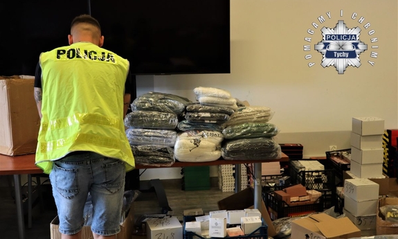 policjant w kamizelce odblaskowej oraz pudełka i kartony z zabezpieczonymi towarami