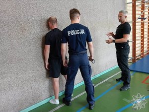 Komisarz Krystian Wieczorek na sali gimnastycznej z dwoma innymi funkcjonariuszami w trakcie zajęć z technik interwencji