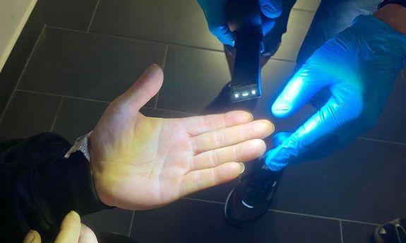 Na zdjęciu widać jak technik policyjny oświetla dłonie zatrzymanemu za rozbój celem sprawdzenia dłoni pod wykonanie daktyloskopii