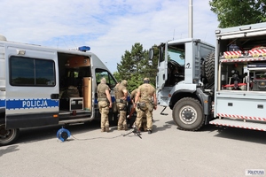 policjanci w moro przyglądają się czemuś stojąc pomiędzy radiowozem a ciężarowym samochodem