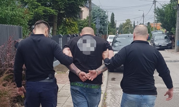 dwaj funkcjonariusze z zatrzymanym mężczyzną idą po chodniku