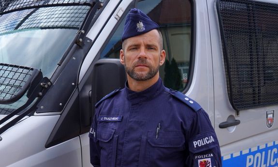umundurowany policjant stoi przed radiowozem