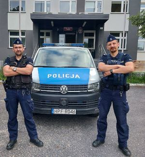 dwaj policjanci stoją przed radiowozem