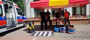 Policjanci i ratownicy medyczni pozują do zdjęcia, przed nimi siedzi pies służbowy po lewej stronie stoi karetka.