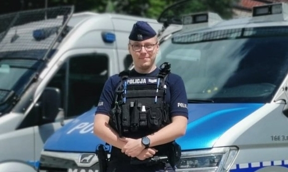 policjant stoi przed radiowozem policyjnym