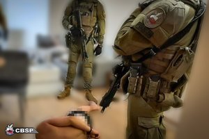 dwaj policjanci CBŚP stoją nad zatrzymanym mężczyzną, który skuty kajdankami leży na podłodze
