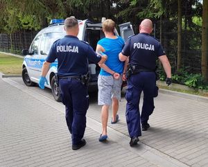 dwaj policjanci prowadzą zatrzymanego mężczyznę zakutego w kajdanki