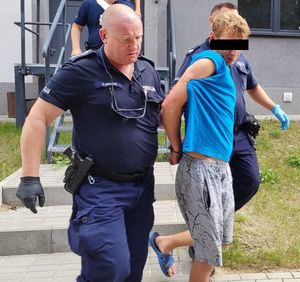 dwaj policjanci prowadzą zatrzymanego mężczyznę zakutego w kajdanki