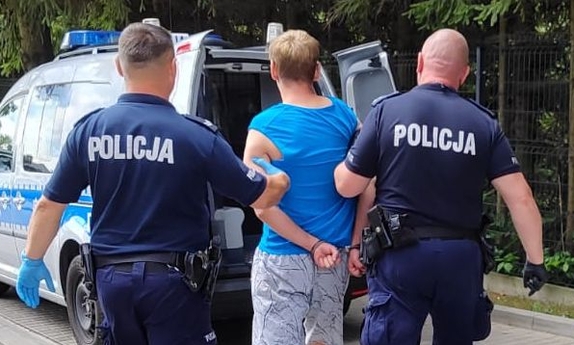 dwaj policjanci prowadzą zatrzymanego mężczyznę zakutego w kajdanki