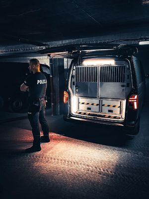 policjant stoi tyłem do busa, który ma otwarty bagażnik