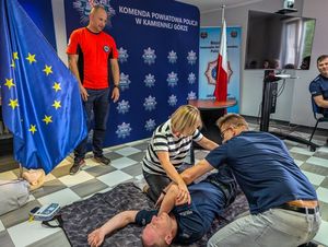 dwie osoby podczas ćwiczeń układają umundurowanego policjanta w pozycji bezpiecznej i przyglądający się temu ratownik który prowadzi szkolenie