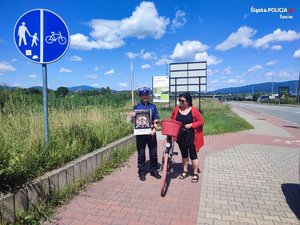 kobieta stojący prze rowerze w czerwonym swetrze i policjantka w mundurze trzymająca obraz