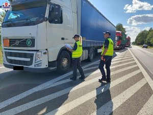 dwaj policjanci w mundurach i odblaskowych kamizelkach kontrolujący samochód ciężarowy