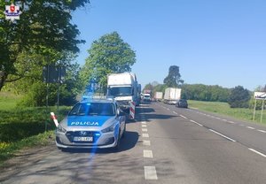 radiowóz z migającymi światłami niebeskimi i stojące za nim trzy ciężarówki