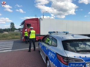 policjanci ruchu drogowego w czasie kontroli ciężarówki, z widocznym na pierwszym planie radiowozem