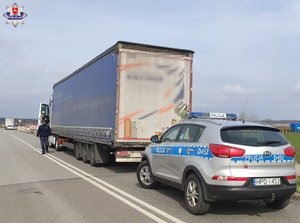 radiowóz stojący za ciężarówką i umundurowany policjant idący w jego kierunku