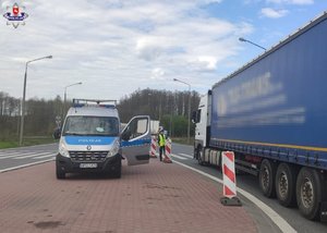 radiowóz z otwartymi drzwiami stojąca przy nim policjantka oraz samochód ciężarowy