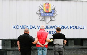policjanci stoją z zatrzymanym przed budynkiem policji
