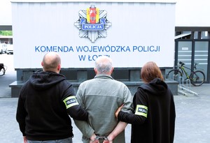 policjanci stoją z zatrzymanym przed budynkiem policji