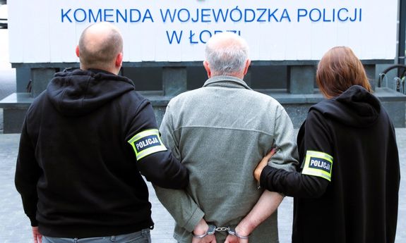 policjanci stoją z zatrzymanym przed budynkiem policji