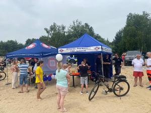 Policjanci w namiocie profilaktycznym rozłożonym na plaży obok namiotu sanepidu, wokół uczestnicy pikniku.