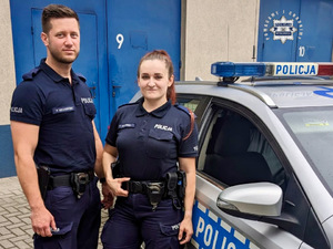 Policjantka i policjant w umundurowaniu stojący przy radiowozie