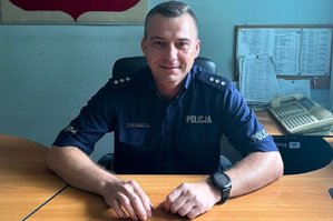 zdjęcie policjanta w umundurowaniu służbowym siedzącego za biurkiem w pomieszczeniu służbowym