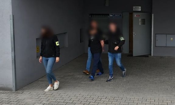 Policjanci wychodzą z zatrzymanym z budynku