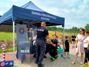 Policjant z grupą dzieci przy stoisku profilaktycznym.