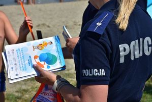 Policjantka trzymając w rękach ulotki akcji &quot;Kręci mnie bezpieczeństwo nad wodą&quot; rozmawia z osobami przebywającymi na plaży.