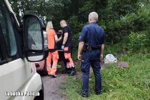 ratownicy i policjant stoją przy samochodzie
