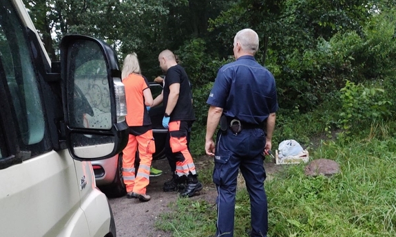 ratownicy i policjant stoją przy samochodzie
