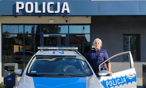 policjantka stoi przy radiowozie, w tle budynek komisariatu Policji