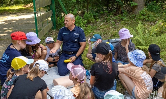 policjant siedzi na trawie z dziećmi i z nimi rozmawia