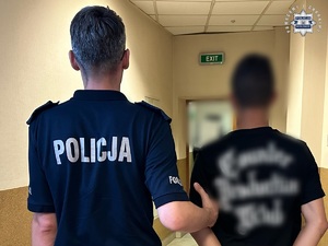 na zdjęciu umundurowany policjant prowadzi zatrzymanego nastolatka
