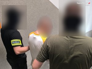 na zdjęciu dwóch policjantów prowadzi zatrzymanego mężczyznę