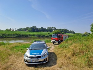 Radiowóz i wóz strażacki stoją nad brzegiem zbiornika wodnego.