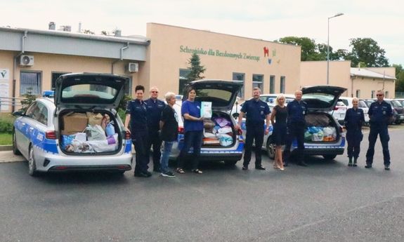 policjanci stoją przy otwartych bagażnikach radiowozów pełnych jedzenia dla zwierząt