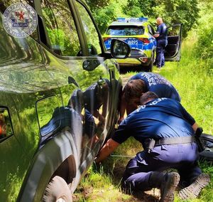 na zdjęciu dwóch umundurowanych policjantów wymienia koło w pojeździe osobowym