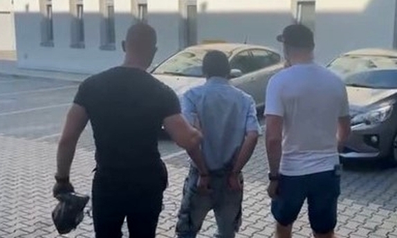 dwaj policjanci prowadzą zatrzymanego mężczyznę zakutego w kajdanki