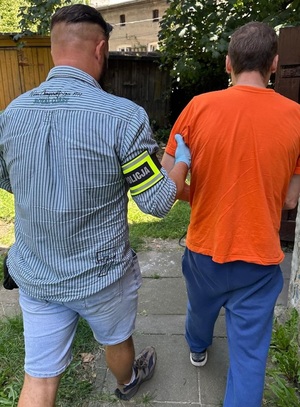 Policjant z opaską z napisem Policja prowadzi zatrzymanego