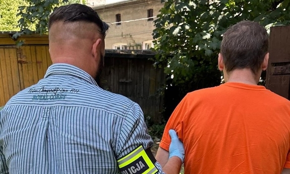 Policjant z opaską z napisem Policja prowadzi zatrzymanego