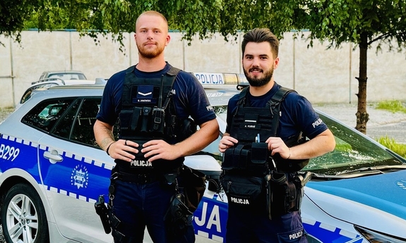 dwaj policjanci stoją przy radiowozie