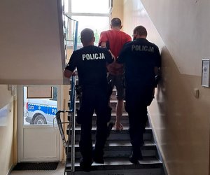 Policjanci prowadzą zatrzymanego po schodach w budynku