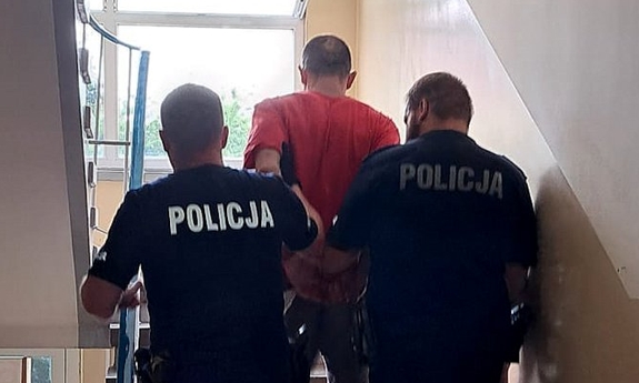 Policjanci prowadzą zatrzymanego po schodach w budynku