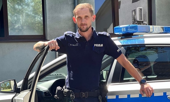 policjant stoi przy radiowozie policyjnym