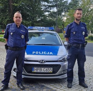 na zdjęciu dwóch umundurowanych policjantów stoi przy radiowozie