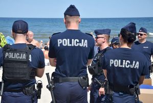 Policjanci odwróceni tyłem w tle plaża i morze.