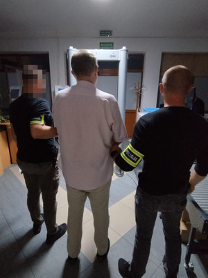 dwaj funkcjonariusze z zatrzymaną osobą zakutą w kajdanki