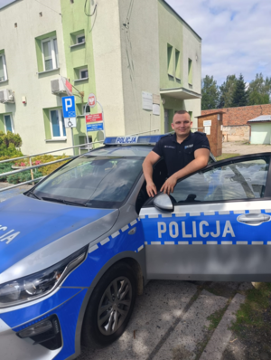 policjant stoi przy radiowozie policyjnym, w tle budynki